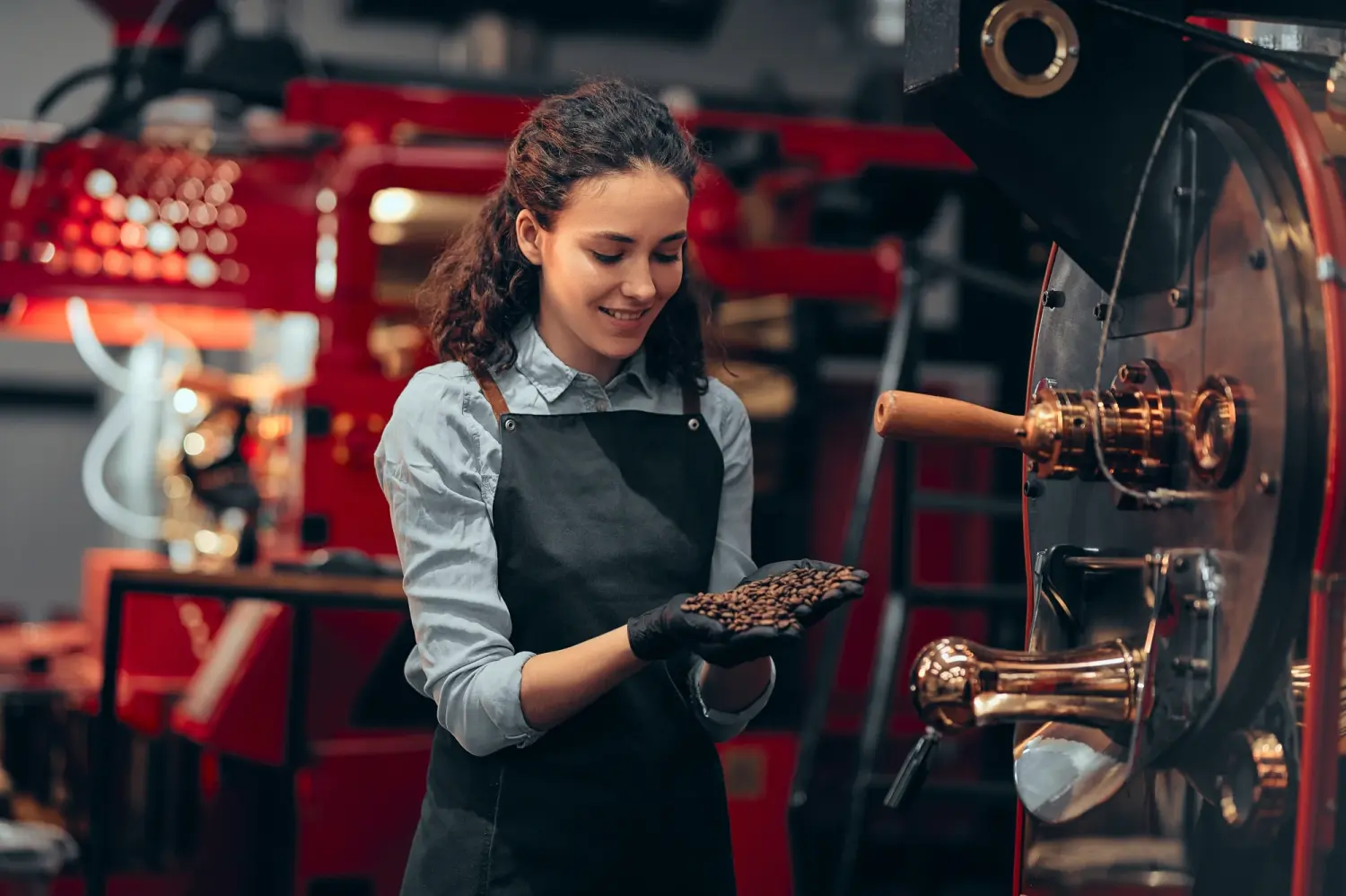 Tress Kaffee, Eine Frau prüft die Qualität der Kaffeebohnen in der Nähe der Röstmaschine in der Kaffeerösterei. Mischen von geröstetem Kaffee.
